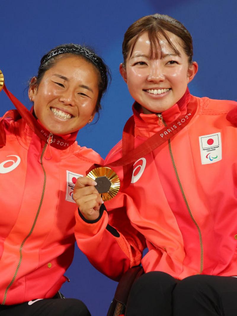 Two female athletes celebrate on the podium with gold medal